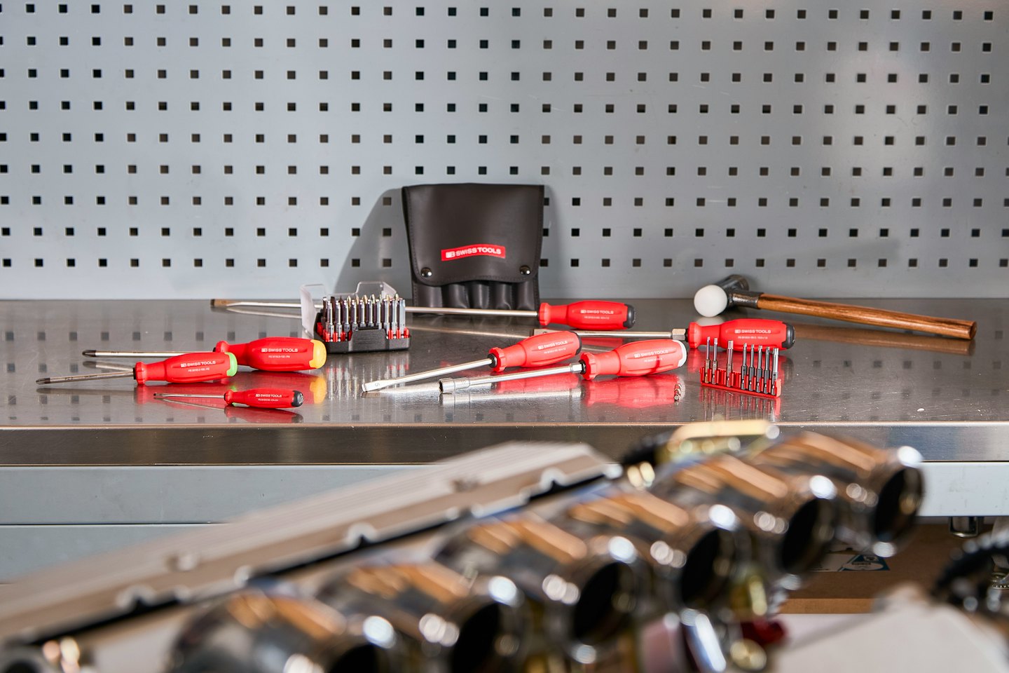 Red-handled screwdrivers and bit sets on a metallic workbench.