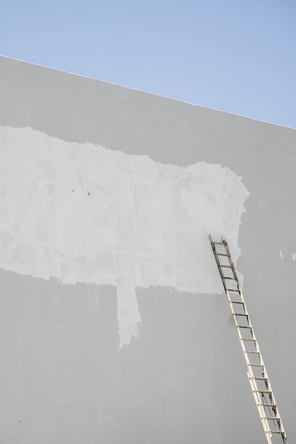 An aluminum ladder leans against a partially painted wall.